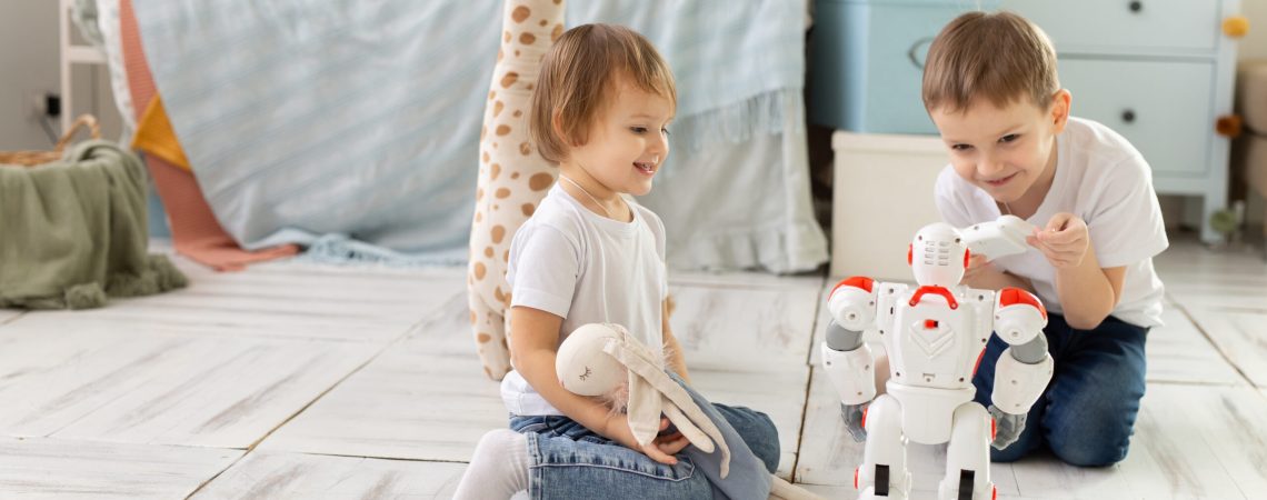 Small children brother and sister sit on the floor in the room, laughing and playing with the robot