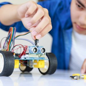 Young asian teen plugging energy and signal cable to sensor chip of toy car workshop.